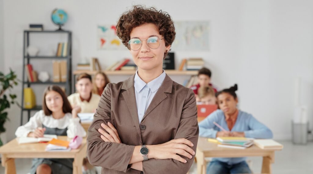 A confident teacher stands in front of students in a classroom setting.
